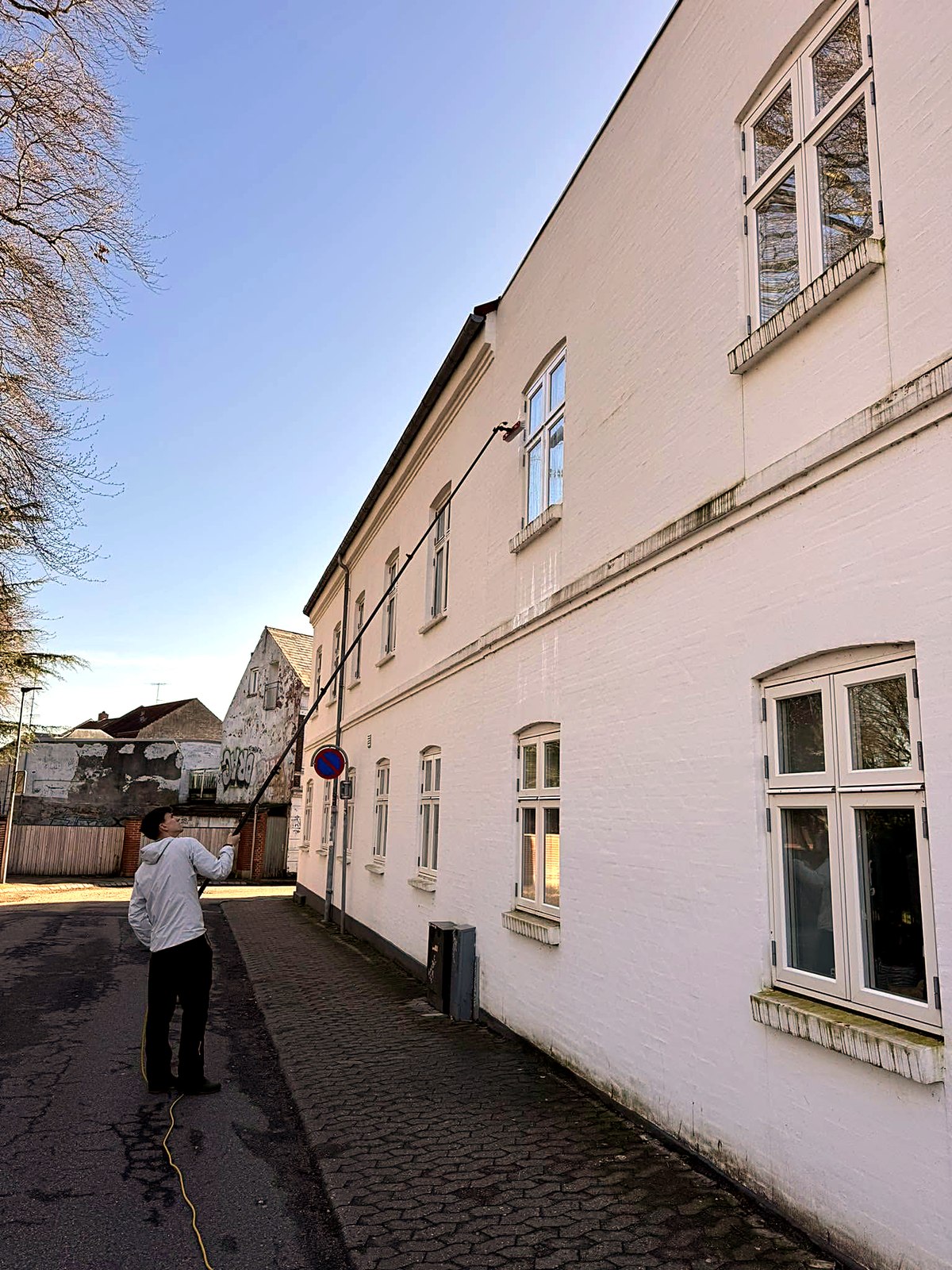 Vinduespolering med teleskopstang og rentvandsanlæg på en høj bygningsfacade